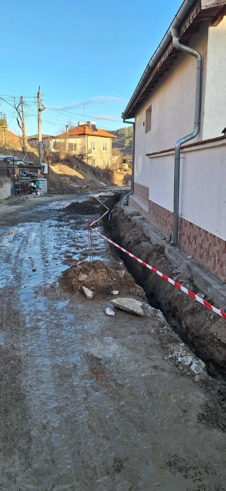Изкоп на траншея покрай къща със сигнална лента, зимни условия